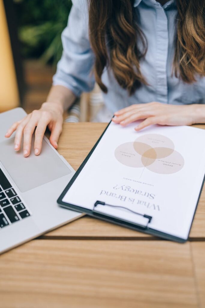 A woman examining a brand strategy document on a clipboard next to a laptop in an office setting.